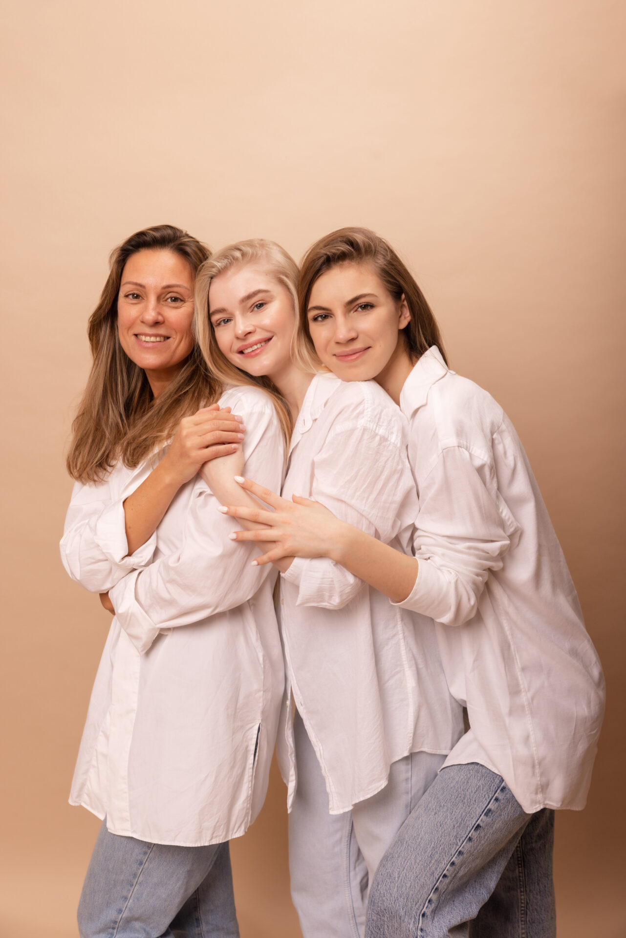 tres-mujeres-jovenes-piel-clara-camisas-blancas-sonrien-camara-abrazandose-si-contra-fondo-beige-concepto-belleza-femenina